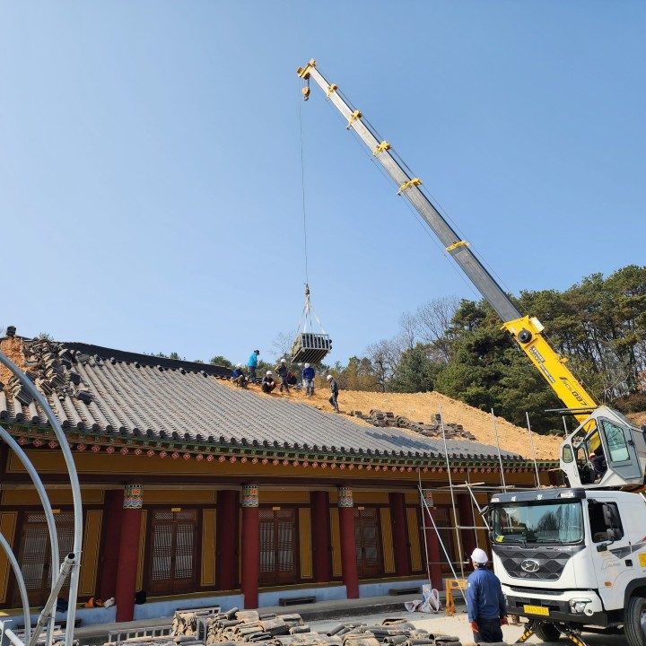 대형 크레인과 다수의 베테랑 기술진이 투입되어 대형 사찰 전통 기와 지붕을 시공하는 현장 사진